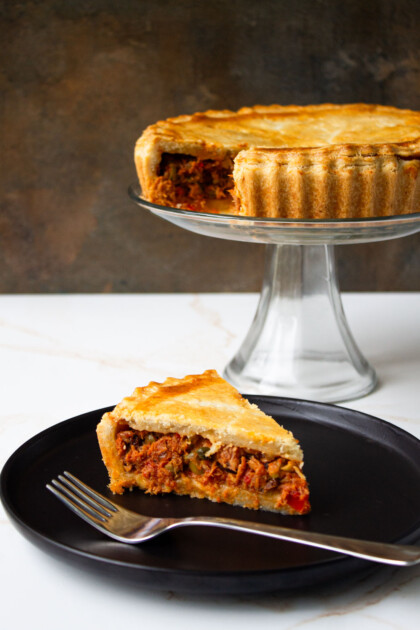 Tuna Polvorosa on a glass cake plate and a piece of the same savory pie on a black dish with a fork.