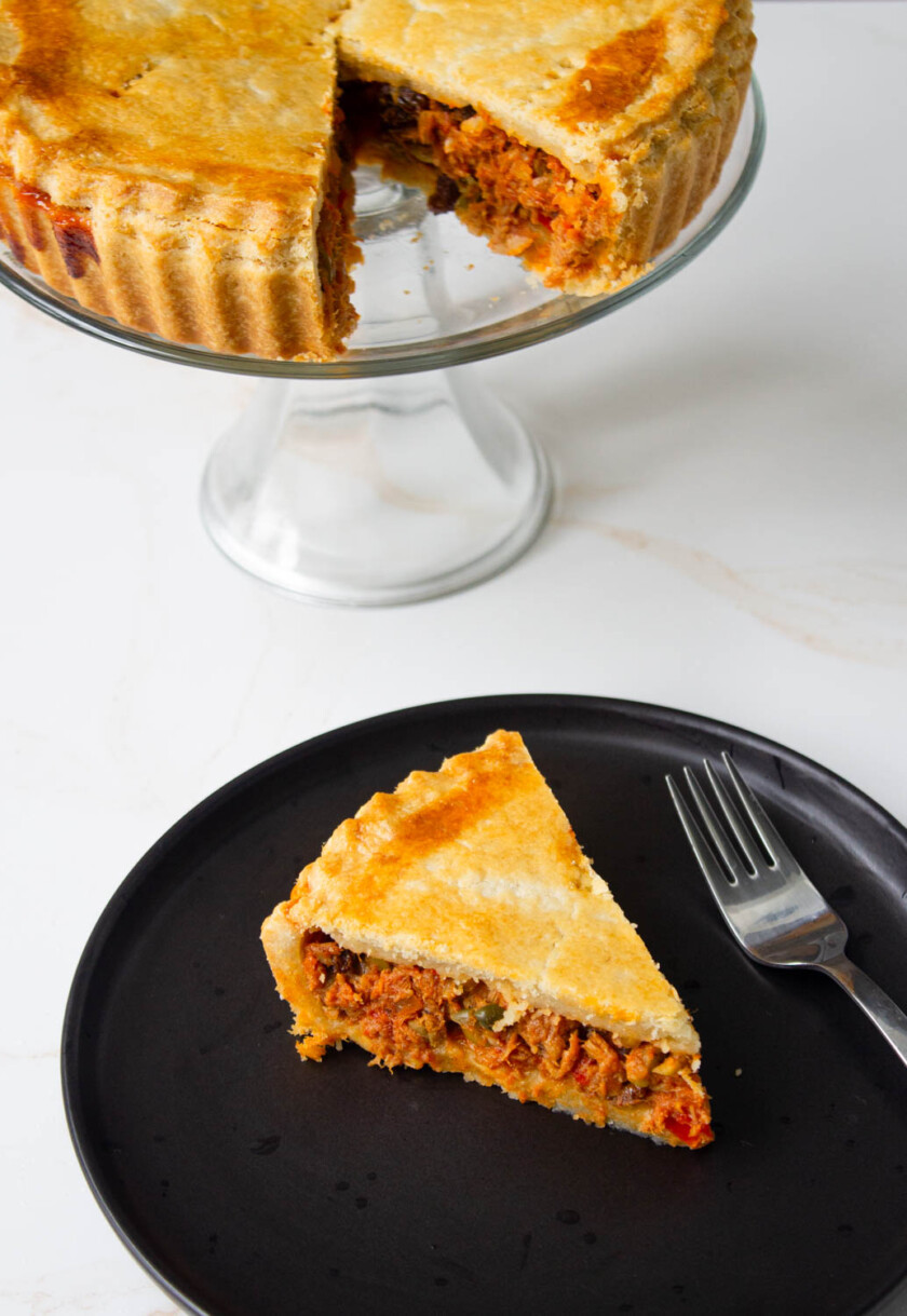 A slice of Tuna Polvorosa, aka tuna pot pie on a black dish with a work, and the pie already cut.