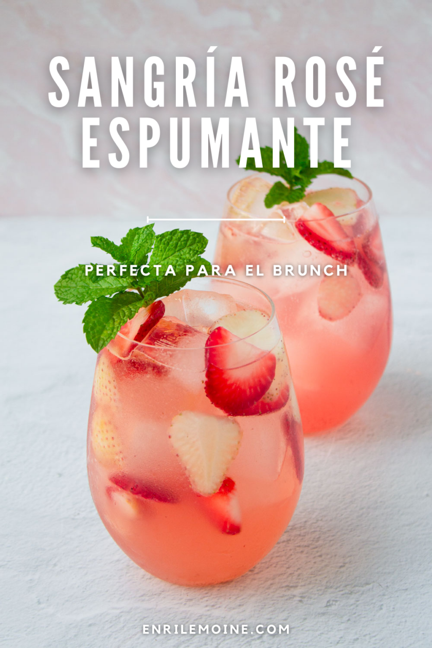 Dos vasos de sangría rosada con fresas y decorados con una ramita de menta.