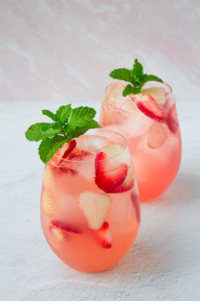 Dos vasos de sangría rosada con fresas y decorados con una ramita de menta.