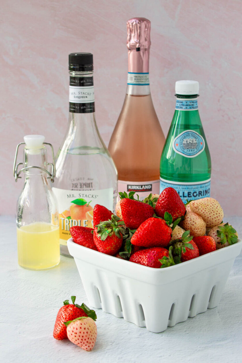 Ingredientes para hacer una sangría rosé espumante, incluyendo Prosecco rosado, triple sec, agua carbonatada, jarabe de limón y fresas