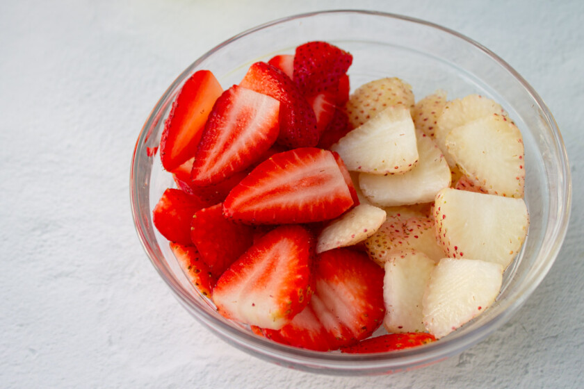 A bowl of fresh sliced strawberries, including pink strawberries.