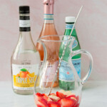 Una selección de ingredientes para un cóctel que incluye fresas frescas, una botella de triple sec, vino espumoso y jarabe de limón.
