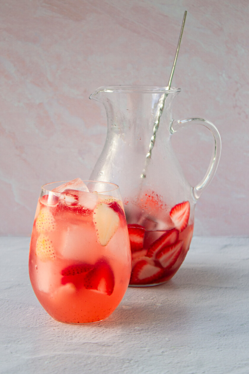 Una jarra y un vaso de sangría rosé.