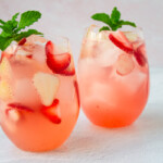 Dos vasos de sangría rosé con fresas, adornados con hojas de menta.