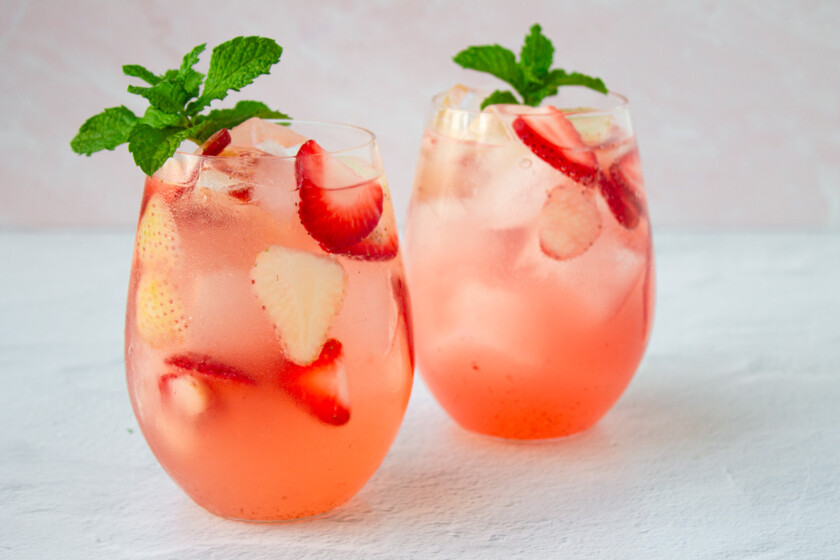 Dos vasos de sangría rosé con fresas, adornados con hojas de menta.