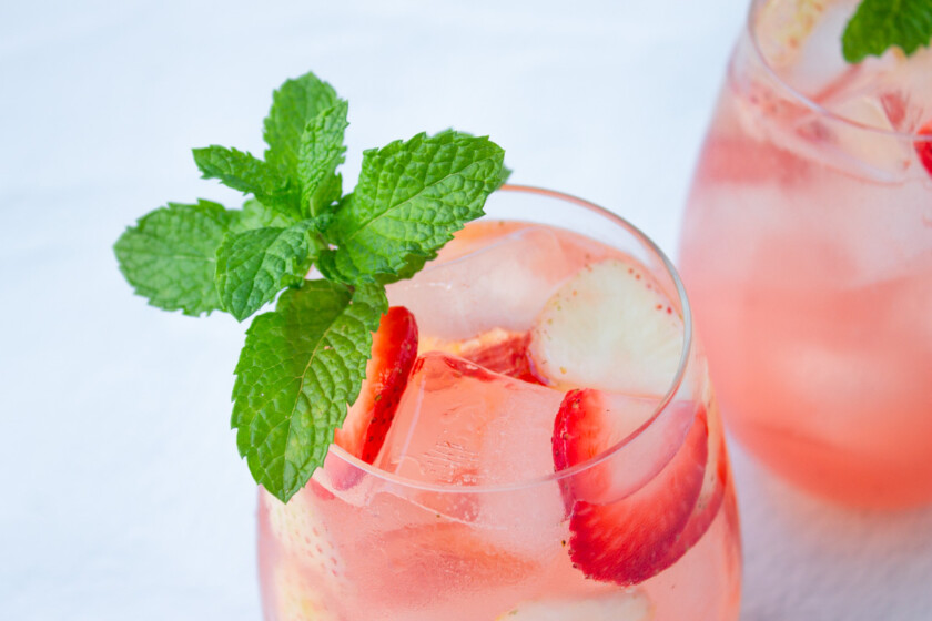 Dos vasos de sangría rosé con fresas, adornados con hojas de menta.