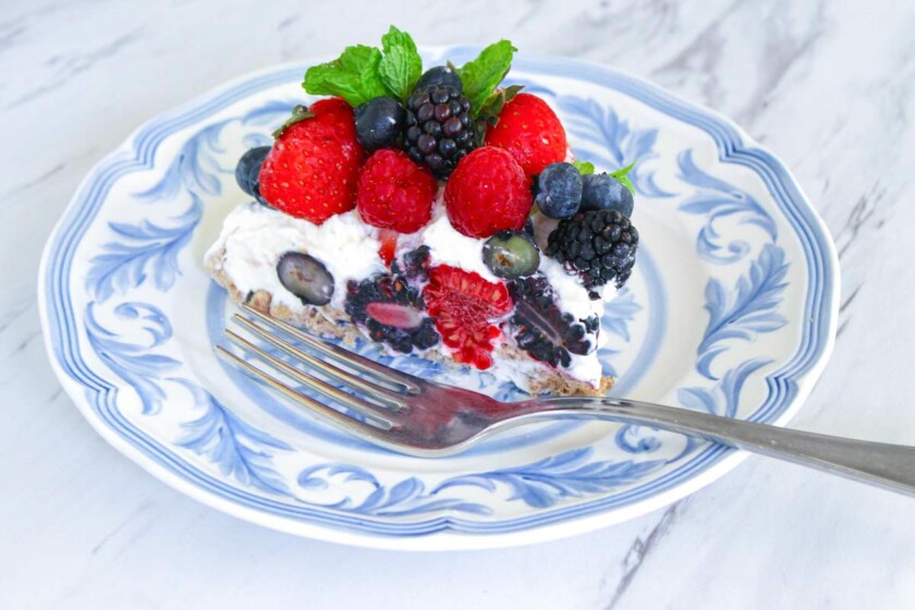 Un trozo de pavlova de frutos rojos mixtos con fresas, frambuesas, moras y arándanos en un plato decorativo blanco y azul, con un tenedor al lado de la tarta.