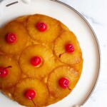 Pastel de piña al revés con rodajas de piña caramelizada y cerezas en un plato blanco.