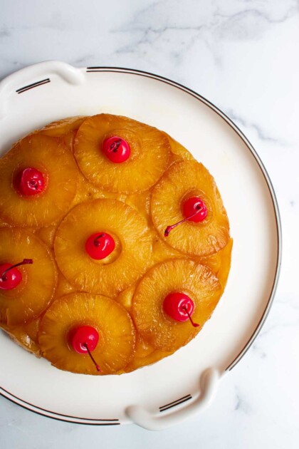 Venezuelan Pineapple upside-down cake, topped with sweet pineapple rings and red cherries on a white plate.