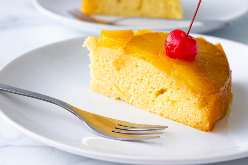 Torta-de-piña-volteada-by-enrilemoine-15 Un trozo de pastel de piña volteado, servido en un plato blanco con un tenedor a un lado.