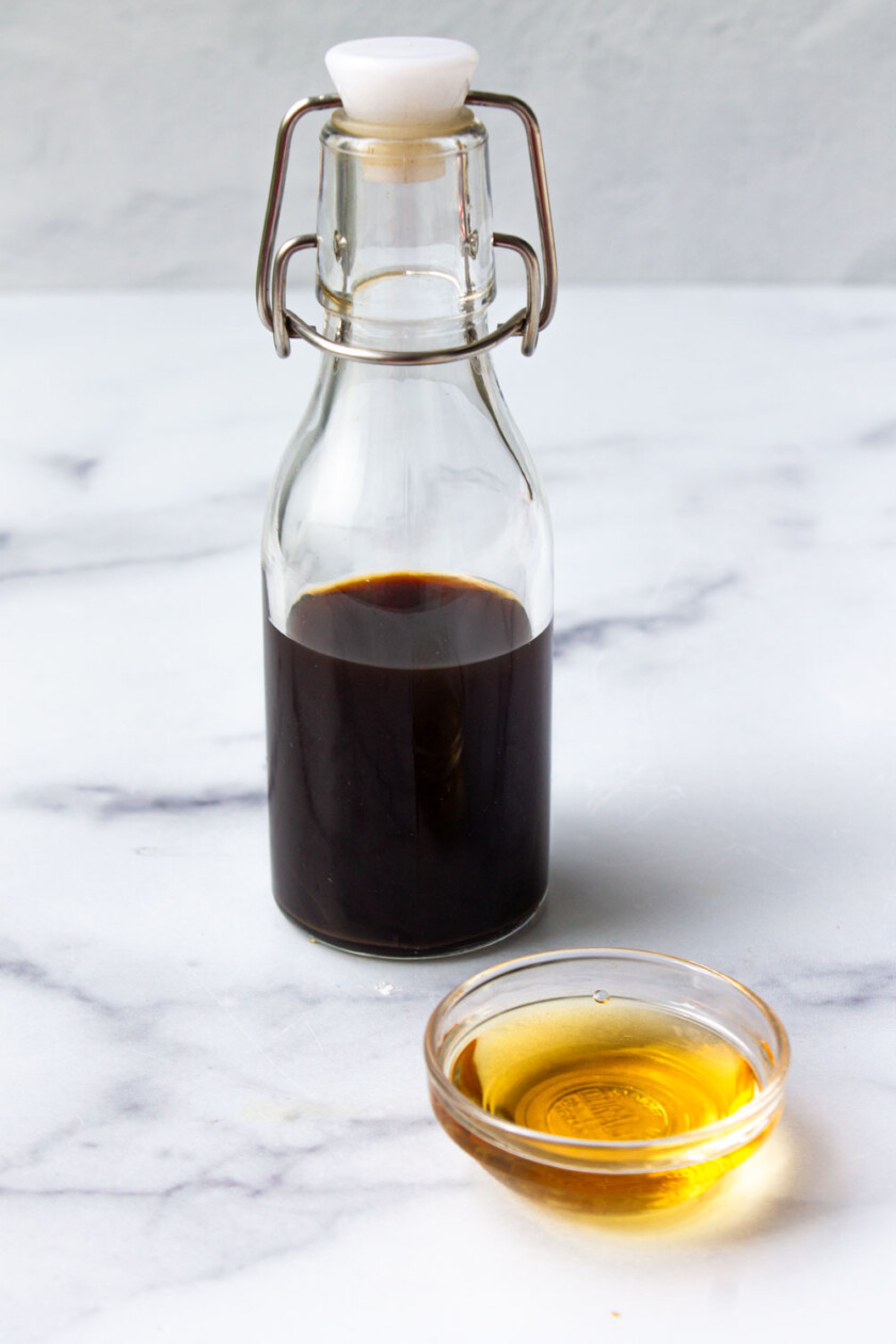 Torta-de-piña-volteada-by-enrilemoine-5 Una botella de vidrio llena de extracto de vainilla y un pequeño recipiente de vidrio con líquido ámbar, ambos colocados sobre una superficie de mármol.