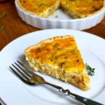 Una rebanada de quiche de cebolla en un plato blanco con un tenedor al lado, y el resto de la quiche en un molde para pastel al fondo.