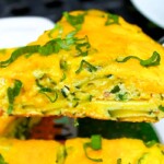 Una rebanada de frittata vibrante con hierbas verdes encima, expuesta en un plato blanco.