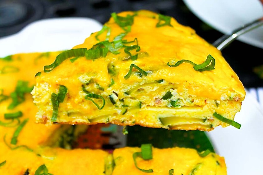 Una rebanada de frittata vibrante con hierbas verdes encima, expuesta en un plato blanco.
