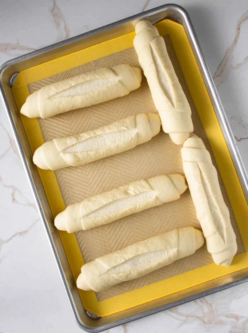 Seis bollos de pan crudos colocados en una bandeja de horno forrada con un tapete de silicona.
