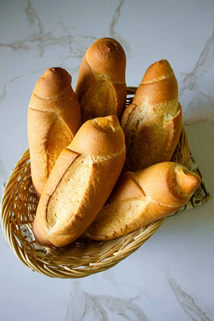 Una cesta de mimbre contiene cinco baguettes recién horneadas dispuestas sobre una encimera de mármol.