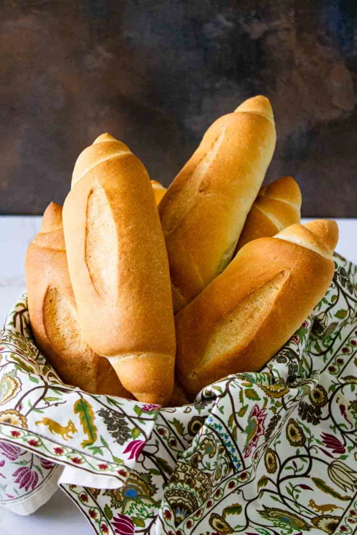 Una cesta con una tela colorida sostiene varias baguettes doradas recién horneadas en posición vertical sobre un fondo oscuro.