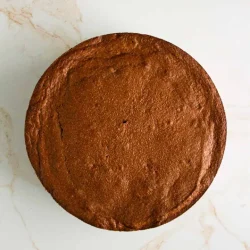 Vista superior de un pastel de chocolate horneado redondo colocado sobre una superficie de mármol blanco.