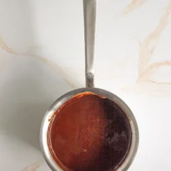 Una cacerola pequeña de acero inoxidable con asa, que contiene chocolatre derretido.