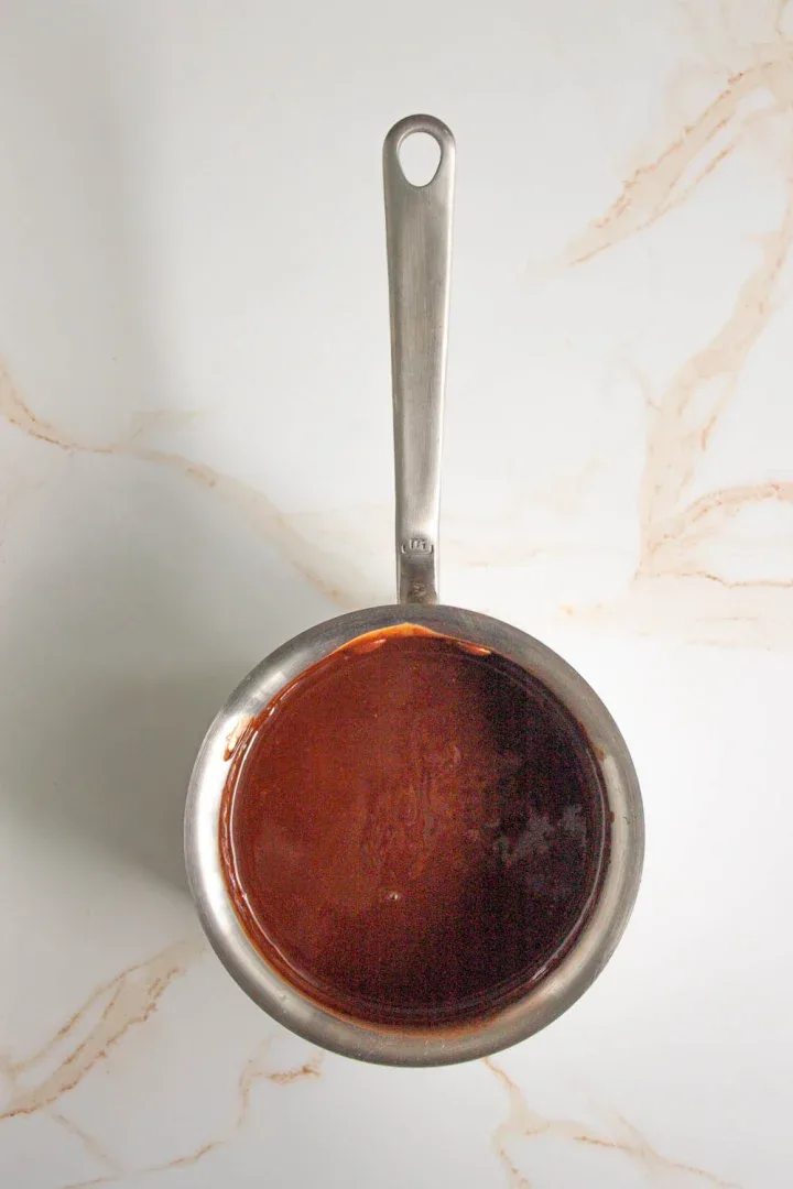 Una cacerola pequeña de acero inoxidable con asa, que contiene chocolatre derretido.