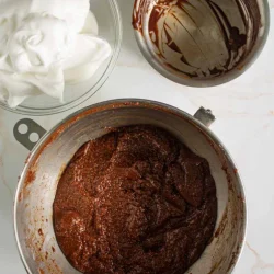 Tres tazones para mezclar que contienen mezcla de chocolate, claras de huevo batidas y restos de chocolate en la encimera de la cocina.