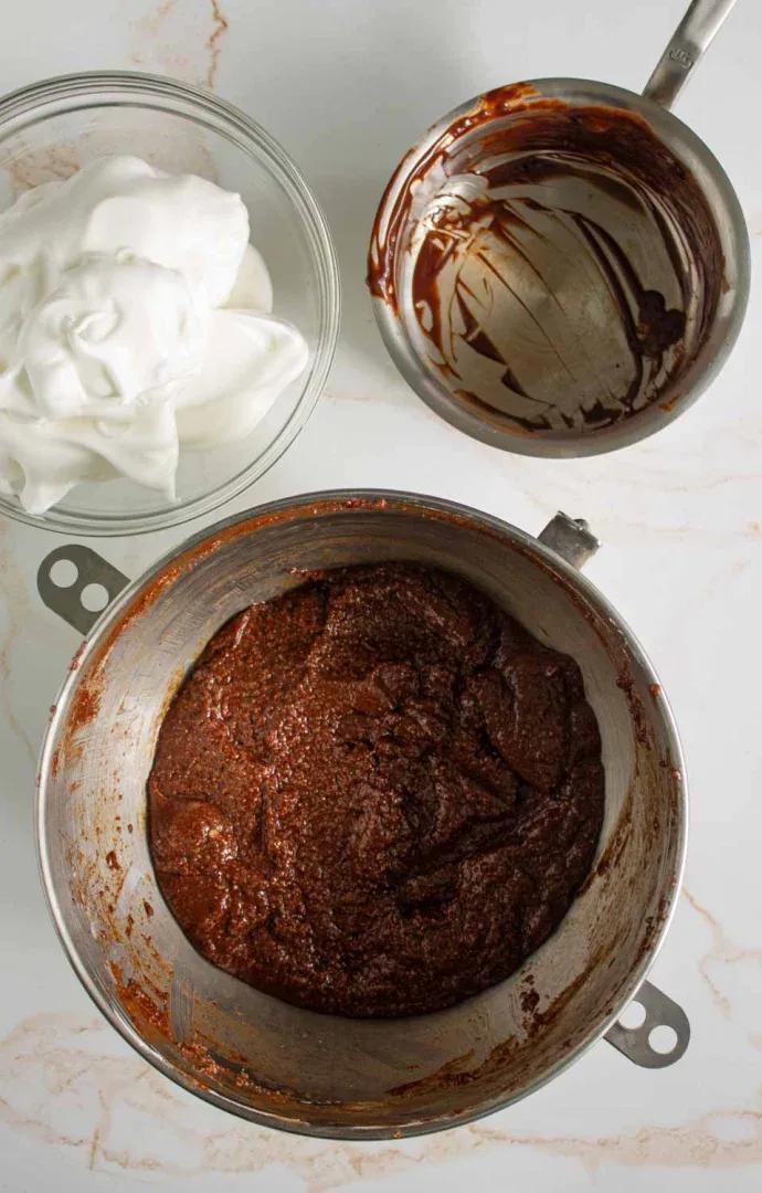 Tres tazones para mezclar que contienen mezcla de chocolate, claras de huevo batidas y restos de chocolate en la encimera de la cocina.