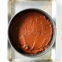 Un molde para pastel redondo relleno con masa de pastel de chocolate reposa en una bandeja para hornear de metal rectangular.