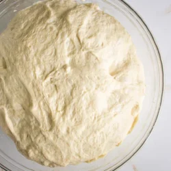 Un recipiente de vidrio lleno de masa cruda que reposa sobre una encimera de mármol blanco.