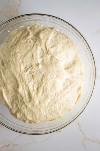 Un recipiente de vidrio lleno de masa cruda que reposa sobre una encimera de mármol blanco.