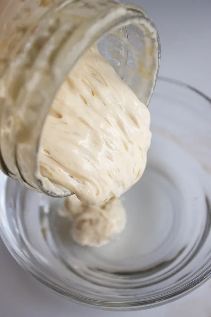 Primer plano de un tarro de masa madre. La masa madre está siendo servida en un tazón de vidrio con agua.