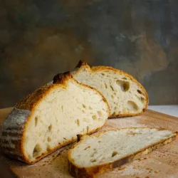 A sliced loaf of rustic sourdough bread on a wooden cutting board, with one piece laid flat.