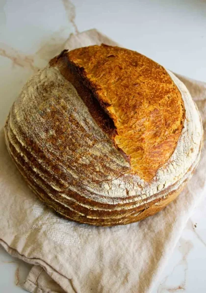 Hogaza redonda de pan artesanal de masa madre, crujiente sobre un paño beige, con una parte superior marcada y una corteza de color marrón dorado.