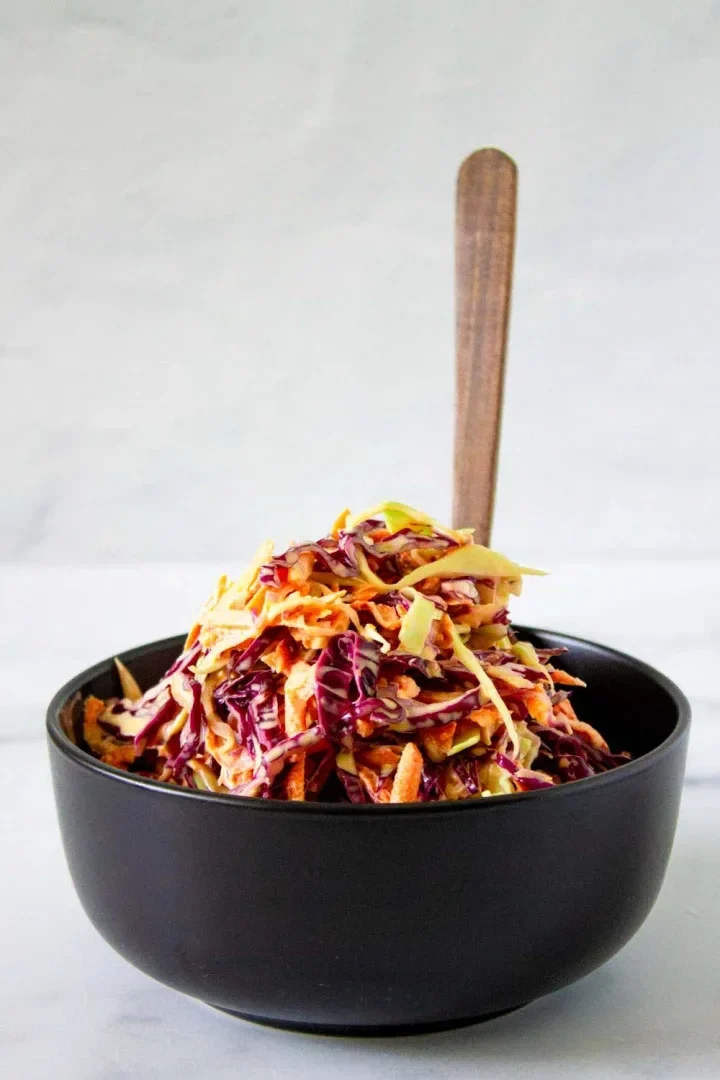 Un cuenco negro lleno de ensalada rallada de zanahoria y repollo.