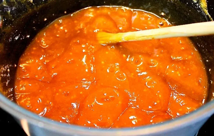 Thick guava jam simmering in a pot, stirred with a wooden spoon.