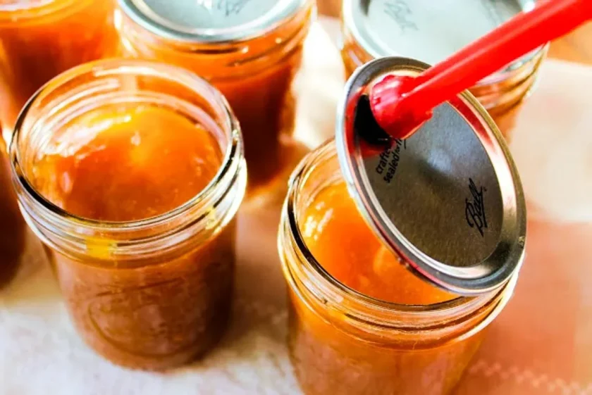 A hand places lids on glass jars filled with guava jam.