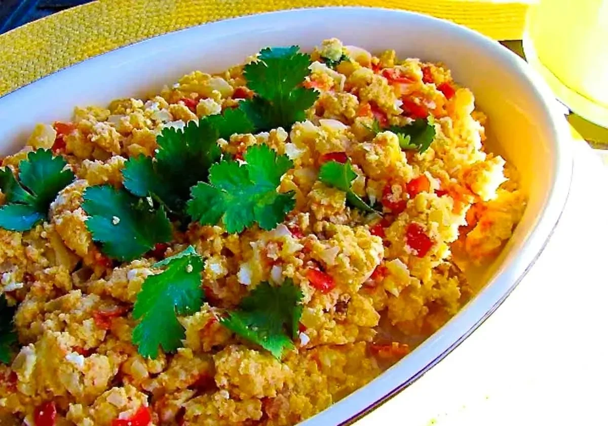 Un plato blanco relleno de huevos revueltos mezclados con tomates, cebollas, hierbas y adornado con cilantro fresco.