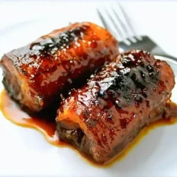 Dos trozos de plátano caramelizados, servidos en un plato blanco, al lado de un tenedor.