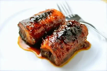 Dos trozos de plátano caramelizados, servidos en un plato blanco, al lado de un tenedor.