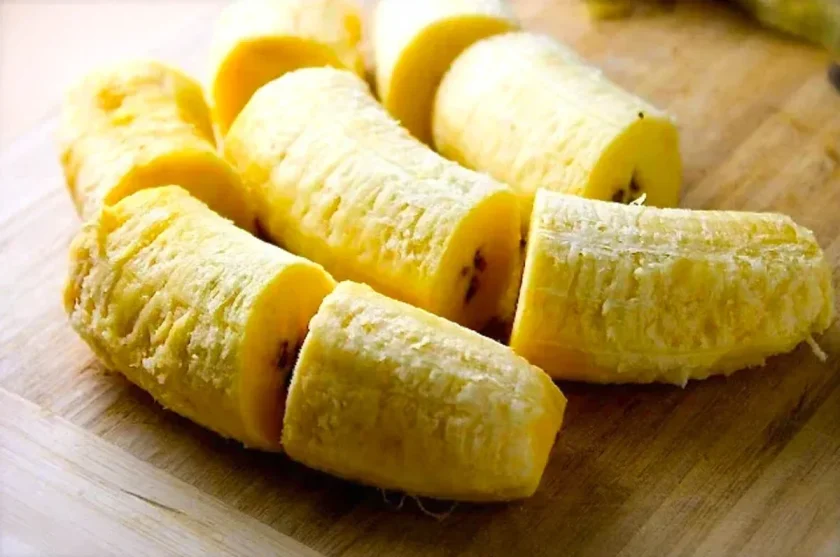 Plantains cut into thirds on a wooden cutting board.