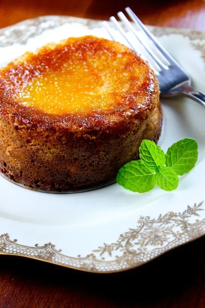 Mini torta de queso criolla caramelizada en un plato decorativo con una ramita de menta y un tenedor al lado.