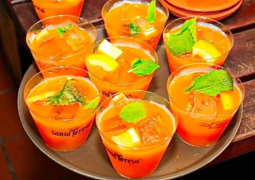 Siete vasos de guarapita de ron y parchita con hielo, hojas de menta y trozos de limón. Los vasos son desechables y están en una bandeja redonda marrón.