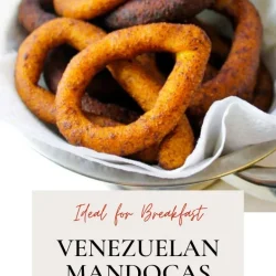 A bowl of fried Venezuelan mandocas, ring-shaped cornmeal treats, on parchment paper with a label reading "Venezuelan Mandocas Recipe.