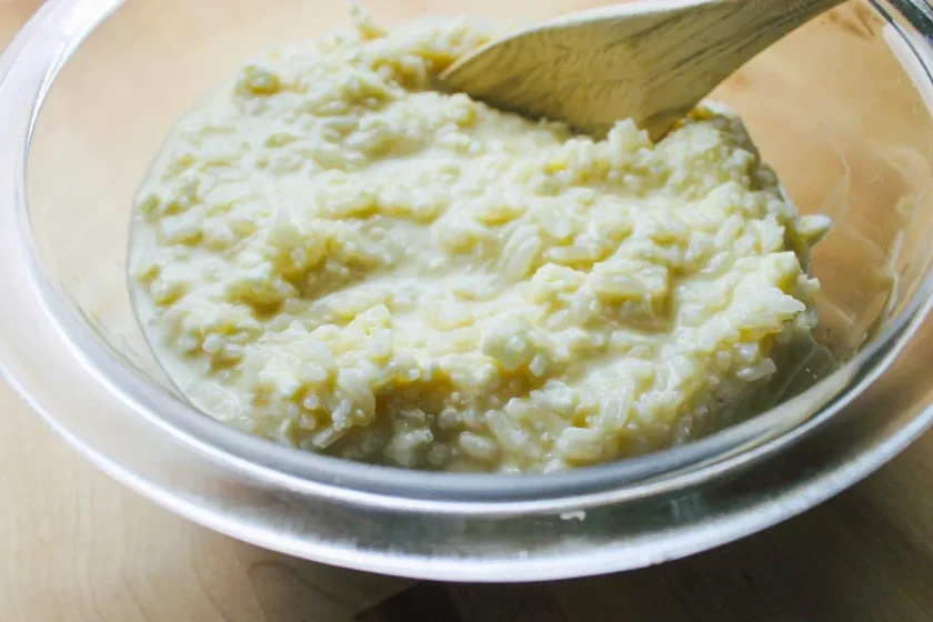 A glass bowl of creamy rice being gently stirred with a wooden spoon.