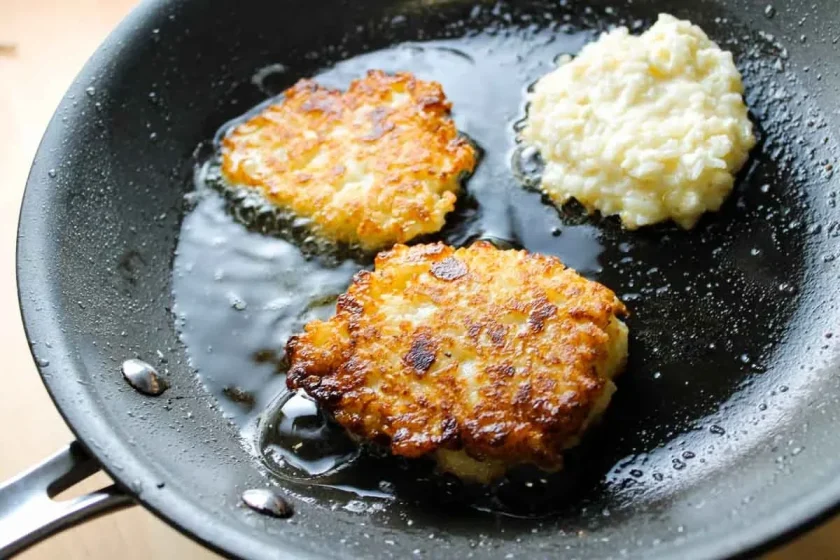 Tres tortitas de arroz friéndose en aceite en una sartén negra, dos doradas y una aún sin cocer.