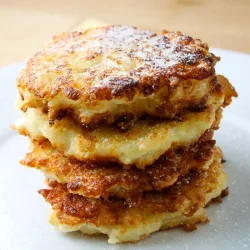 A stack of four golden, crispy rice fritters lightly dusted with sugar on a white plate.