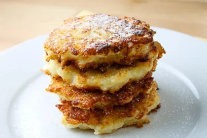 A stack of four golden, crispy rice fritters lightly dusted with sugar on a white plate.