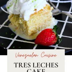 A slice of tres leches cake with meringue and lime zest, served with a strawberry on a black plate.