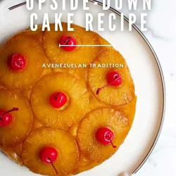 A pineapple upside-down cake, made Venezuelan-style, and topped with cherries, sits on a white plate, viewed from above.