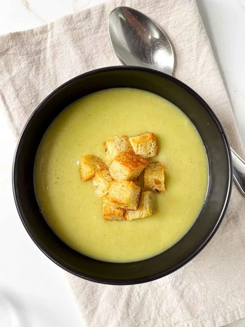 Un cuenco de sopa cremosa de ajo porro con papa, con crutones o picatostes, colocado sobre una servilleta de tela con una cuchara al lado.